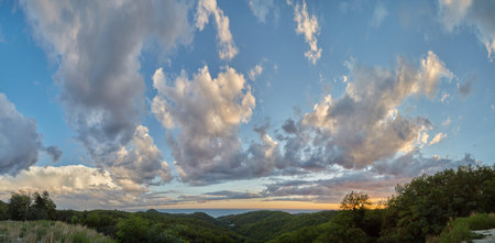 View of green hills near the sea and beautiful cumulus clouds at sunset