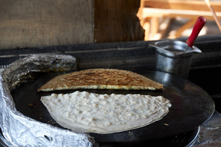 Traditional Turkish gozleme stuffed with meat and cheese are fried on the stove.