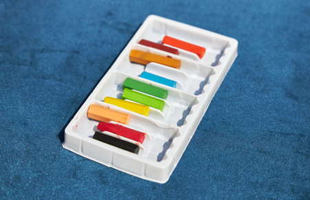 Set of colored crayons in a white box lies on a blue surface.