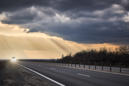 Truck rides on an asphalt road in the background of thunderclouds and rays of the sun.