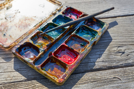 Palette of old mixed paints with a brush lies on an old gray wooden tableの写真素材