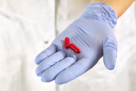 Two red pills in the palm of his hand in a rubber disposable glove.の写真素材