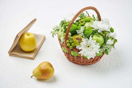 Still life with a wicker basket filled with fruits, white flowers and an open book.の写真素材