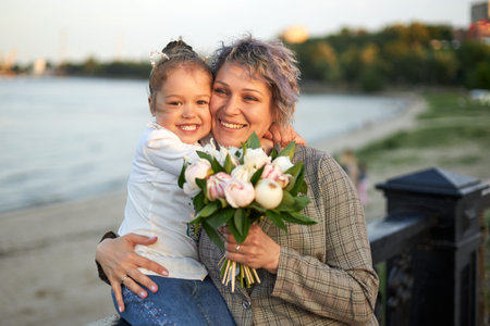 Happy mother and little daughter stand in the evening on the city promenade and laugh