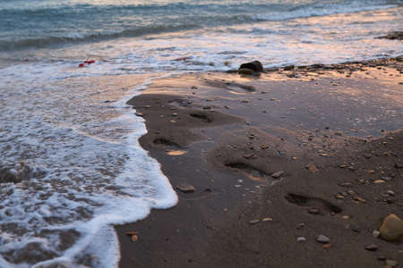 Human footprints on the sand walking in the sea in the eveningの写真素材