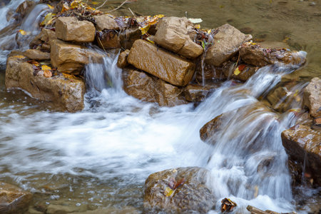 Small stream of water flows through a barrier from large stonesの写真素材