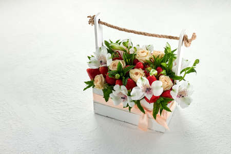 Wooden box filled with ripe strawberries and beautiful white and pink flowers on a white backgroundの写真素材