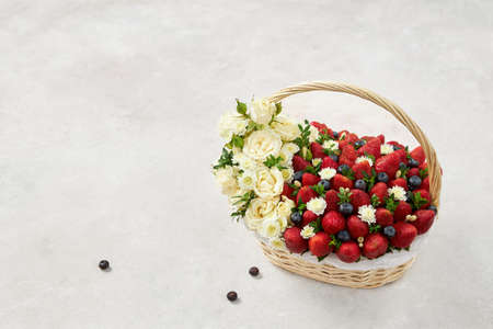 Basket filled with strawberries, blueberries and white flowers on a white backgroundの写真素材