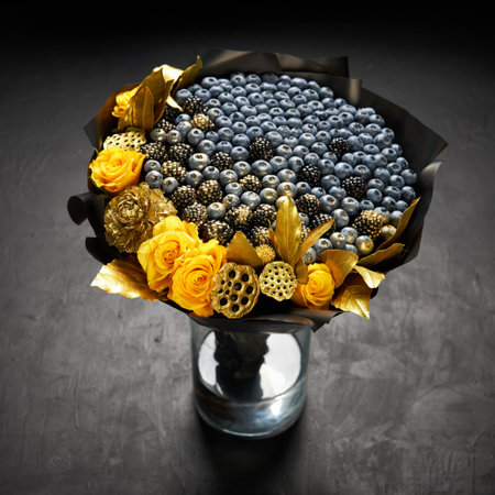 Cool bouquet of blueberries and blackberries decorated with yellow roses and gold leaves standing in a vase on a black backgroundの写真素材