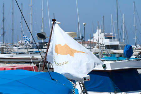 National flag of Cyprus waving at sea harbor in front of moored boats and blue skyの写真素材