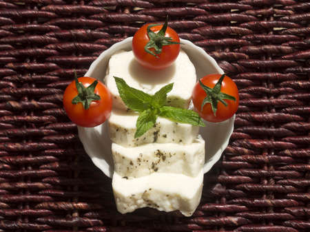 Small bowl with three cherry tomatoes and slices of Cypriot halloumi cheese with fresh mint leaves in sunlight, top viewの写真素材