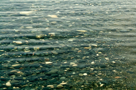 Texture of rippled transparent sea water above beach stones