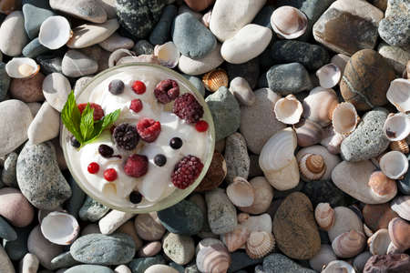 Top view of bowl of vanilla ice cream with berries and mint leaves standing on beach stones in sunlightの写真素材