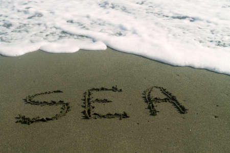 Word Sea written on wet sand at the beach with white foamy waveの写真素材