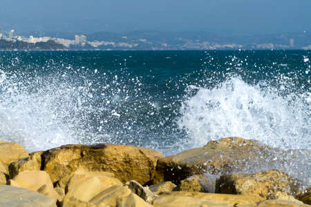 Yellow rocks with white sea wave spray and blurred coastline with mountainsの写真素材