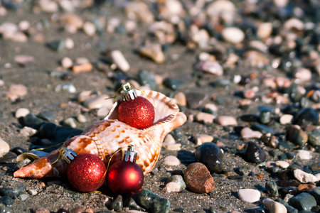 Three red Christmas balls and big seashell at the beach among the sand and pebbles