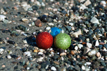 Three colorful Christmas balls at the beach among the sea pebblesの写真素材