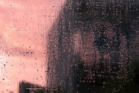 Wet glittering window glass with lots of transparent rain drops and view of pale sky and blurred...