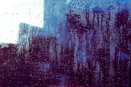 Wet window glass with glittering water drops and abstract blue and purple blurs and silhouettes