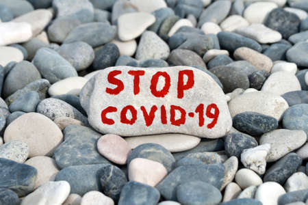 Big white stone with written message Stop COVID-19 laying on the beach among gray pebblesの写真素材