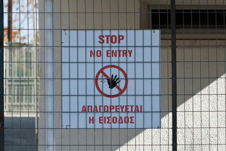 Bilingual no entry signboard in Greek and in English on a metal fence in front of a house wallの写真素材
