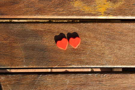 Two red heart shaped figures on brown wooden background in sunlight