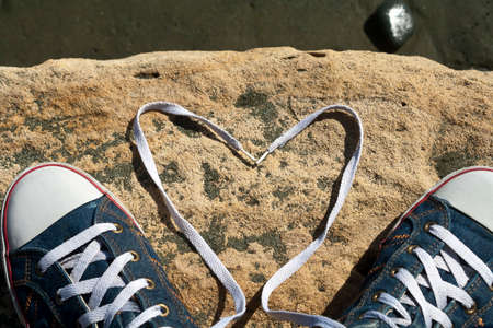 Shoelace heart and a pair of sneakers on a rock in sunlightの写真素材
