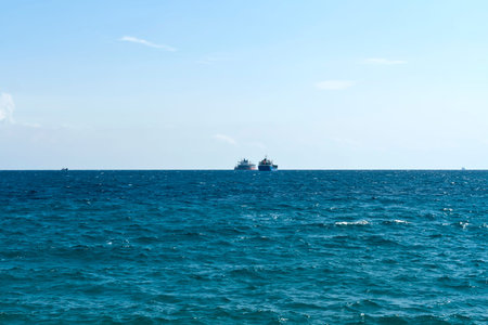 Rippled aquamarine sea water surface, pale blue sky and ships on the horizon