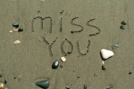 Phrase Miss You written on wet beach sand among stones and pebblesの写真素材