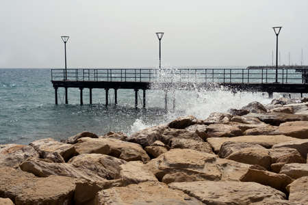 Stone embankment and sea pier on the Molos promenade in Limassol, Cyprus with wave splash and dusty skyの写真素材