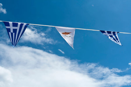 Greek and Cypriot national flags garland in front of blue sky and white clouds