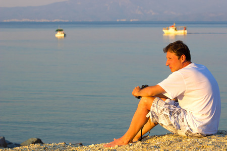 Man looking towards the sea ; Man with binoculars in his hands thoughtfully looking out towards the horizonの写真素材