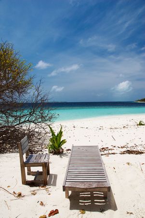 Plank bed and chair on white sand against azure oceanの写真素材