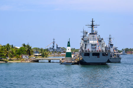 Modern military vessels are docked at a tropical naval base, with a prominent green and white...