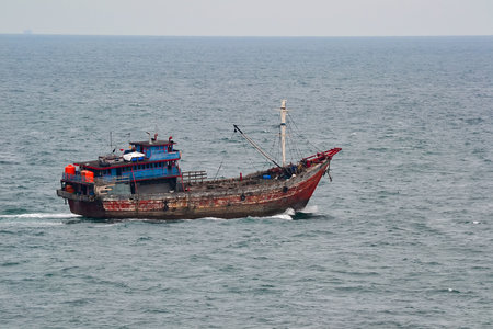A rustic wooden fishing boat with vibrant red and blue paint navigates the open sea, equipped with fishing gear and a small cabin, far from shore.の写真素材