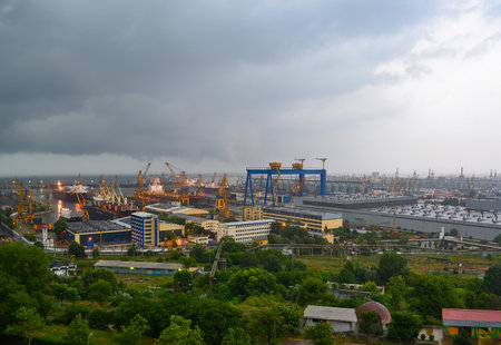 View of Gdansk shipyard in Poland featuring blue gantry cranes, industrial buildings, and waterfront. Overcast skies and greenery create a dramatic contrast.の写真素材