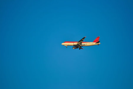 A commercial airplane with red and white colors flies mid flight against a clear blue sky, with landing gear visible, suggesting an approach for landing.の写真素材