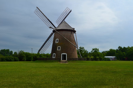 A traditional windmill with a brick base and wooden blades stands in a grassy field, surrounded by...