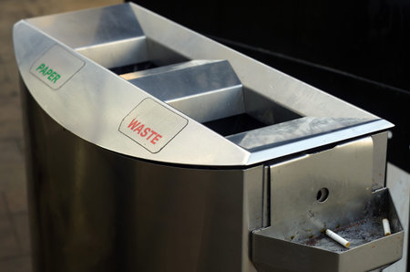Stainless steel waste bin with labeled slots for paper and waste, featuring an attached ashtray with...