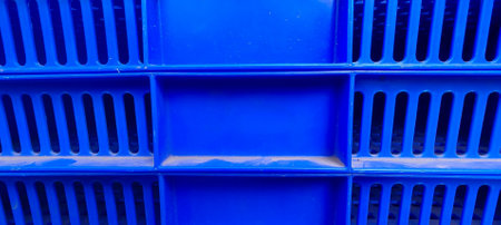 Close up view of a blue plastic crate featuring a grid like pattern with rectangular slits in rows and a solid rectangular section in the center.の写真素材
