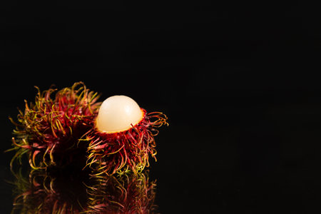 Open and closed rambutans on a mirror surface with a black background and large copy space for text placement.の写真素材