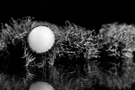 One open and many closed rambutans on a mirror surface with a black background in black & white