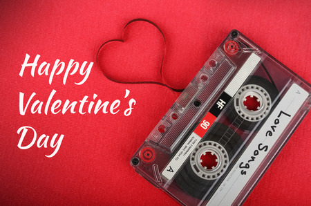 Valentines day card. Vintage audio cassette with loose tape shaping a heart on red backgroundの写真素材