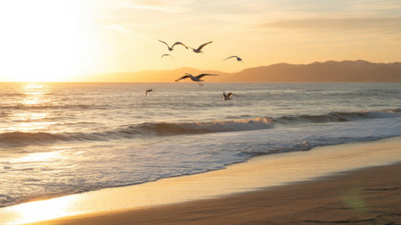 Seagulls fly over the ocean waves as the sun sets, casting a golden glow on the water and mountains.の素材