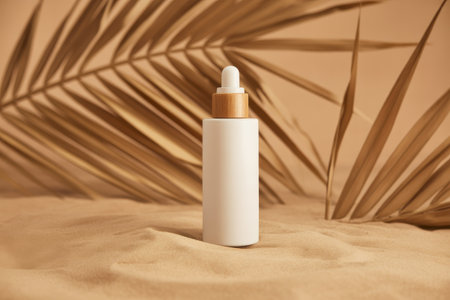 A white dropper bottle with a bamboo cap sits on textured sand. Dried palm leaves cast shadows in the background.の素材