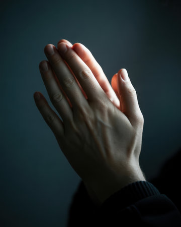 A close-up of hands in a prayer position with soft lighting creating a serene and spiritual atmosphere against a dark backgroundの素材