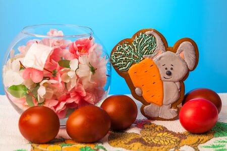 Homemade biscuits with a picture of a rabbit, flowers in a glass vase and Easter eggs on a blue...