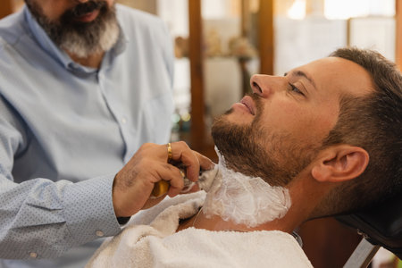 Barber applying shaving soap with a brush on the neck of a man who is going to be shaved with a barber's razor in a barber shop.の写真素材