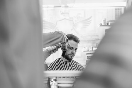 A man is getting his hair cut in a barbershop. The barber is using a pair of scissors to cut the man's hair. The man is looking at the barber, who is focused on his taskの写真素材