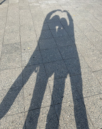 Berlin Germany October 2025 Shadows of two people leaning together on a sunny paved sidewalk